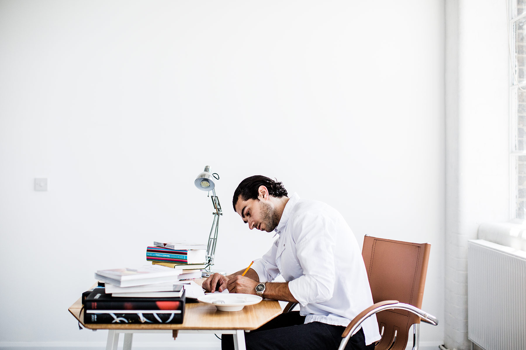 Jozef Youssef writing at a table with books in a bright studio